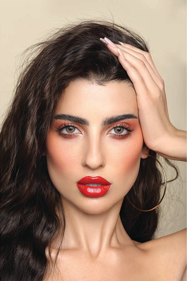 Woman with dark hair and red lipstick against a beige background